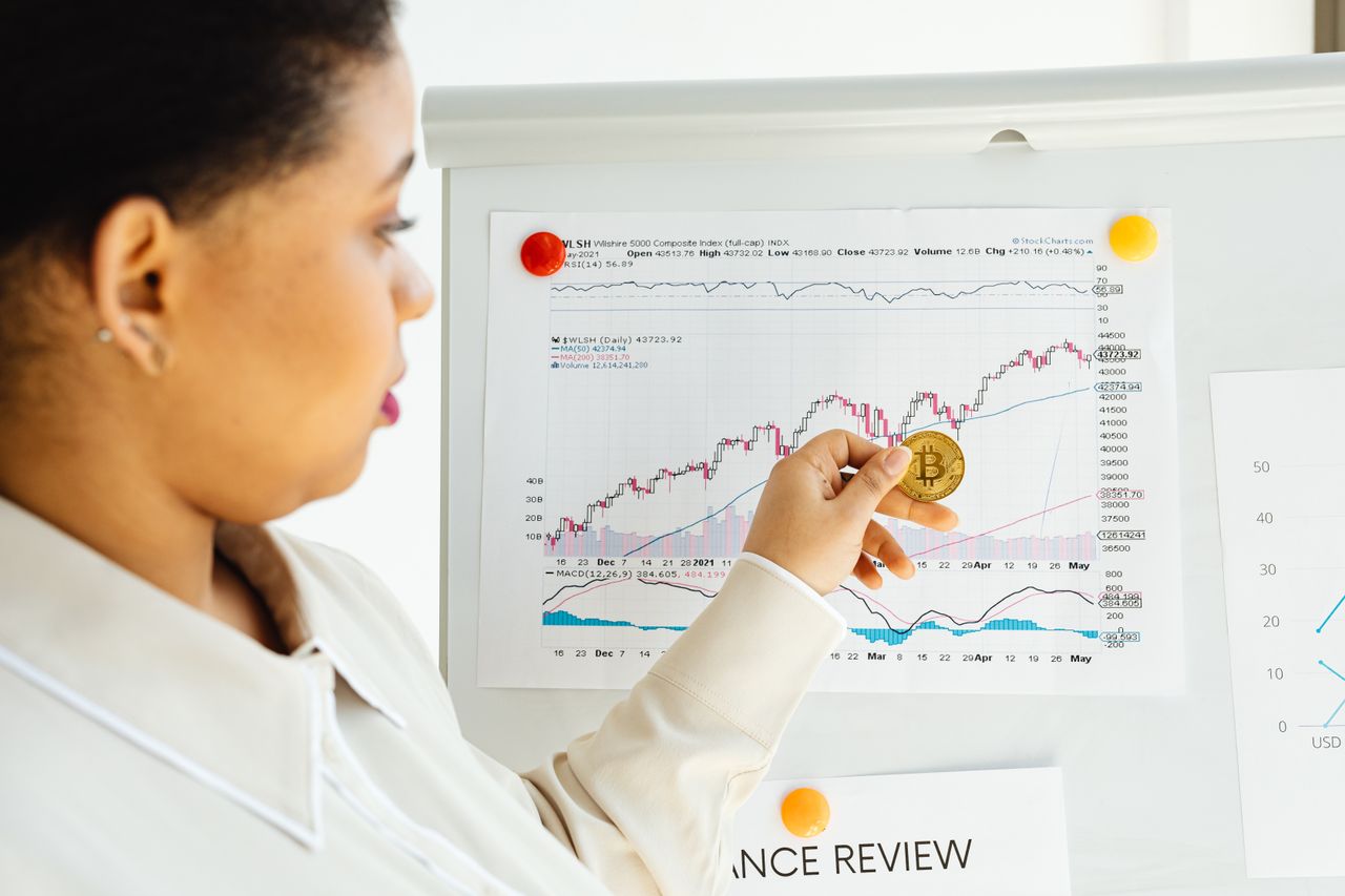 African American woman examines bitcoin and stock market trends on a whiteboard.